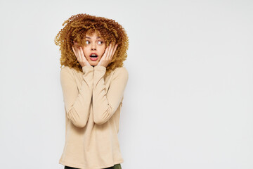 Surprised woman with curly hair expression, light background, neutral colors, showing shock and curiosity, vibrant personality, fashionable casual style, capturing surprise and engagement