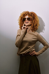 Stylish woman with curly hair in sunglasses posing confidently against a neutral background, exuding a chic and fashionable vibe perfect for lifestyle and fashion themes