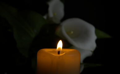 White calla lily flowers and burning wax candle in darkness