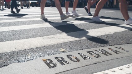 Broadway street sign, people on pedestrian zebra crossroad. New York City Manhattan road intersection. Text on asphalt near crosswalk, shadows on crossroad ped crossing. Traffic signage, United States © Dogora Sun