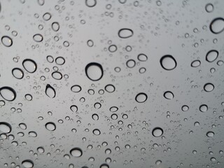 Raindrops, water droplets settle on the glass. There is a blurry image in the background.