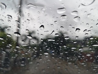 Raindrops, water droplets settle on the glass. There is a blurry image in the background.