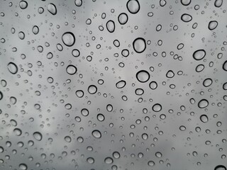 Raindrops, water droplets settle on the glass. There is a blurry image in the background.