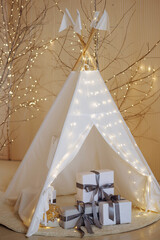 Christmas interior. White wigwam is illuminated with lights, and gifts are stacked inside. New Year's background in beige colors. © Kaplitskaya Love