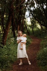 Happy woman holding a small child in her arms in the summer in the park. Concept of motherhood and child care.
