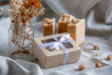 Cute pieces of craft natural soap and a gift box with a white ribbon on a fabric background