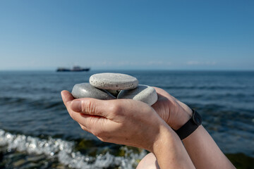 Hands hold pieces of craft soap in the shape of stones against the background of the sea or Lake Baikal. Concept of the image of organic cosmetics against the background of nature