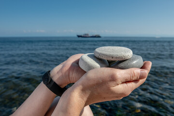 Hands hold pieces of craft soap in the shape of stones against the background of the sea or Lake Baikal. Concept of the image of organic cosmetics against the background of nature