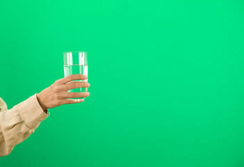 Woman hand holding glass of water on green background.