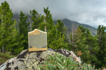 Piece of craft soap on the background of mountains, forests and sky. Concept of the image of organic cosmetics in a natural environment