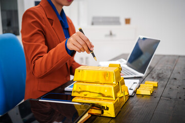 An Asian businesswoman is sitting at her desk in the office,analyzing gold bullion prices,market trends,investment factors,providing in-depth analysis adjust trading strategies for positive returns.
