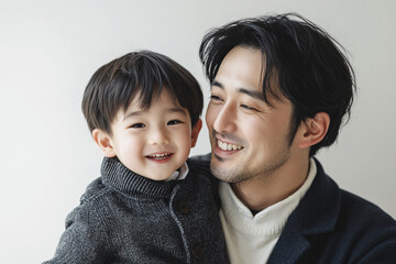 Obraz premium Loving father and young son smiling and sharing joyful moments, either looking at each other or at the camera, in a cozy white studio setting, capturing heartwarming family interactions.