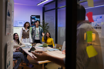 Group of young Asian professionals collaborating on a late-night project meeting in a modern...