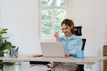 Young Professional Woman Working from Home, Celebrating Success at Desk with Laptop in Bright Modern Home Office