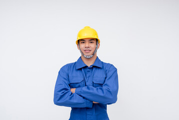 Confident young construction worker wearing blue coveralls and a yellow hard hat, standing against...