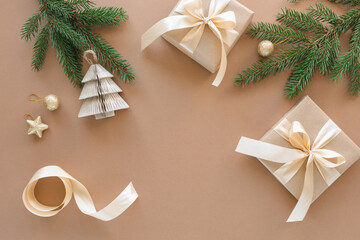 Overhead view of two wrapped Christmas gifts, fir branches, Christmas ornaments on a beige background.
