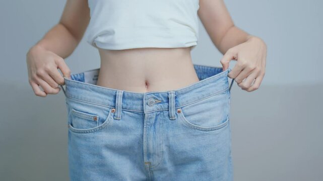young slim female wearing big or oversize jeans, woman show healthy shape after weight loss. dieting, exercise, body fit and liposuction surgery concept