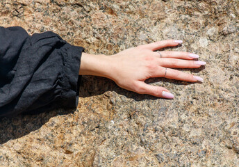 A woman's hand is resting on a rock, with her nails painted