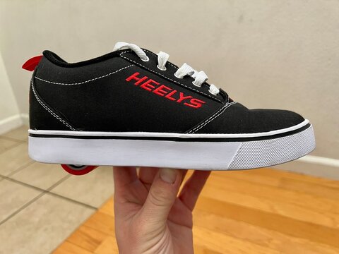Holding a single Heely's brand skating shoe in black with white sole.