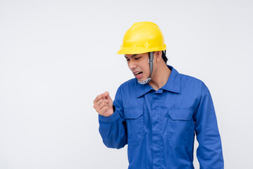 A young construction worker in blue coveralls and a yellow hard hat examines his injured finger. on...