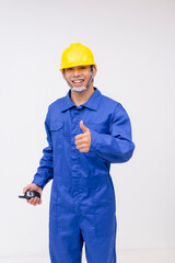 Energetic young construction worker in blue coveralls, isolated on white, holding a two-way radio and giving a thumbs-up gesture, conveying positivity and readiness.