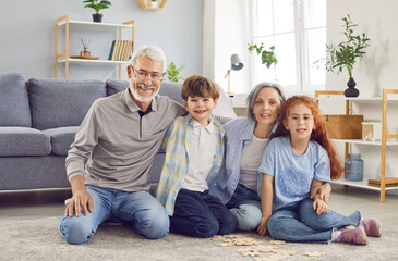 Loving elderly senior and grandchildren at home, grandmother, grandfather family have fun with little children, happy caring mature grandparents spend time, posing sitting at living room floor 