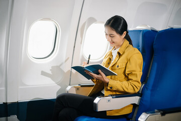 Attractive Asian female passenger of airplane sitting in comfortable seat while working laptop and tablet. Travel in style, work with grace.