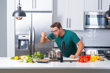 Man cooking at kitchen. Handsome man preparing delicious meal in modepn kitchen. Male chef cooking...