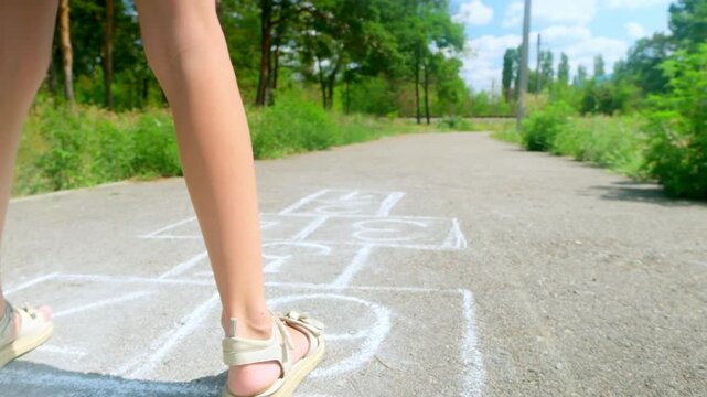 Close-up of a little girl feet and hopscotch drawn on the asphalt. A child plays hopscotch games on an outdoor playground on a sunny day. Summer activities for children.