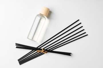 A minimalist display of essential oil and black diffuser sticks on a clean white background