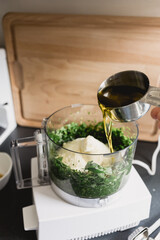 Person adding olive oil into a food processor to make pesto
