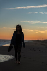 Fototapeta premium Silhouette of a woman walking along the seashore as the sun sets.
