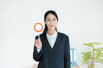 マルの札を持つスーツを着た女性