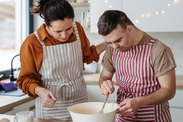Young man with Down syndrome and his mom preparing dough for Christmas cookies. Christmas peaceful moment for man with Down syndrome.