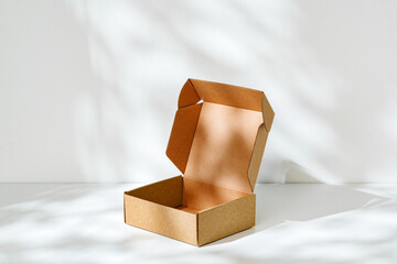 An open cardboard box rests on a bright white surface with soft shadows highlighting its edges and structure in natural light