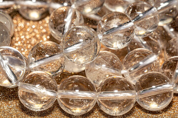 Natural clear quartz, rock crystal. Round shaped beads for DIY jewelry design. Macro photo over rose gold glitter background.