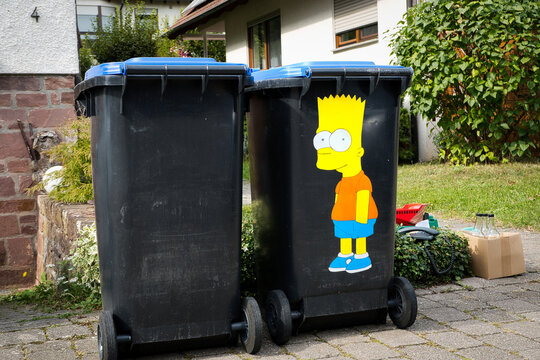 Zwei M&uuml;lltonnen mit blauem Deckel f&uuml;r Altpapier, von denen eine mit Bart Simpson bemalt ist