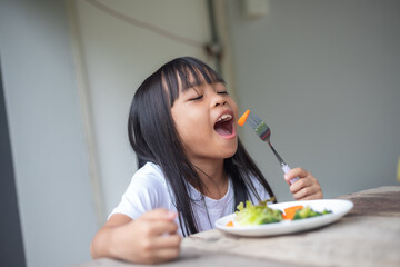 A young girl is sitting at a table with a plate of vegetables in front of her.