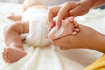 Unrecognizable woman applying cream to her baby’s small legs while massaging gently with careful hands to provide comfort and care for the infant’s soft skin