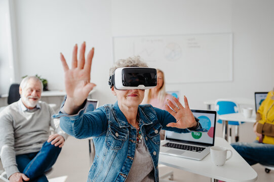 Group of seniors with VR goggles on computer and technology education class. Elderly people learning about virtual reality, using VR headset.