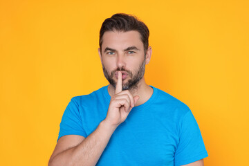 Shh man. Portrait of man showing shh taboo sign with finger to lips over yellow studio background....