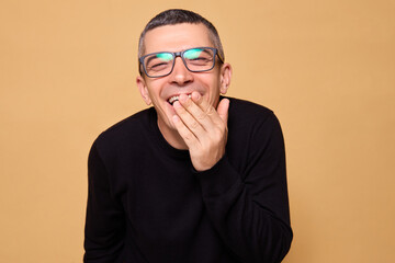 Joyful man wearing black raglan and glasses laughing out loud and covering mouth enjoying funny...