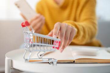 A close-up of a woman touching a mini shopping cart model on a table. shopping online, lifestyles