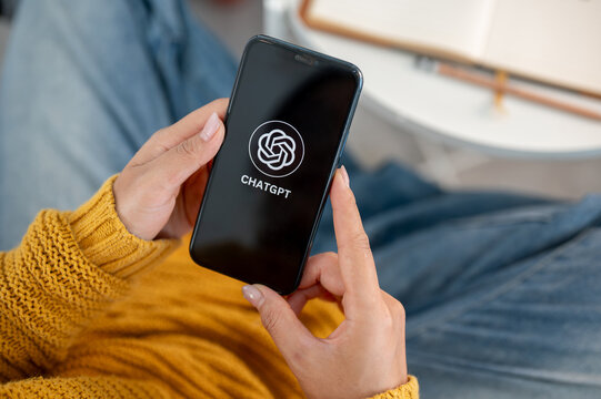 A close-up of a woman using the ChatGPT application on her iPhone while sitting on a couch at home.