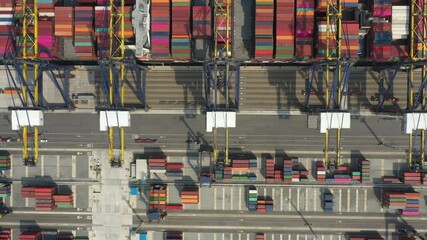 Aerial showing a container ship navigating into a busy industrial port. Cranes and shipping containers highlight global trade in motion