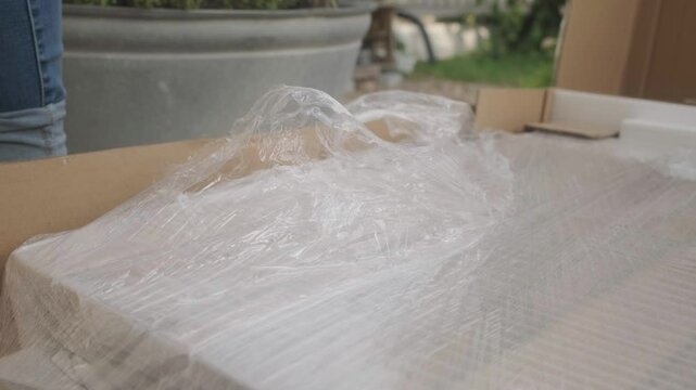 Low angle documentary shot of a female opening a package with a box cutter, cutting the foil and removing it, building furniture for outside.