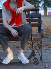 Golden autumn with a young athlete in a red hoodie on his shoulders, sitting on a bench with a...