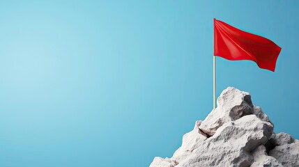 A vibrant red flag proudly waves atop a rocky peak against a clear blue sky, symbolizing achievement and ambition.