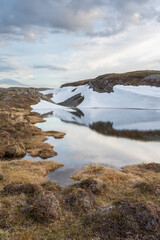 A small pond in the mountains on a calm and windless early summer day with lingering snow on the slope, Vardø, Varanger Peninsula National Park