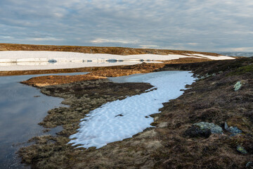 Lingering snow and a small pond in the highlands of Varanger Peninsula National Park in the warm light of a summer night, Vardø